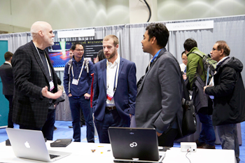 Attendees talk to an innovator about his products while other attendees mingle in the background.